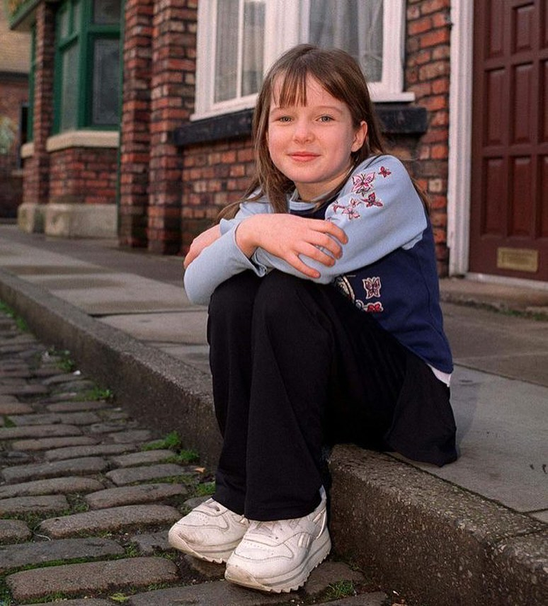 Girl sitting on a curb outside a brick building.