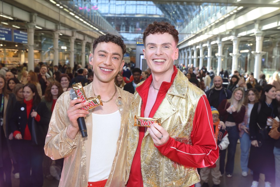Two men in gold jackets holding Twix candy bars.