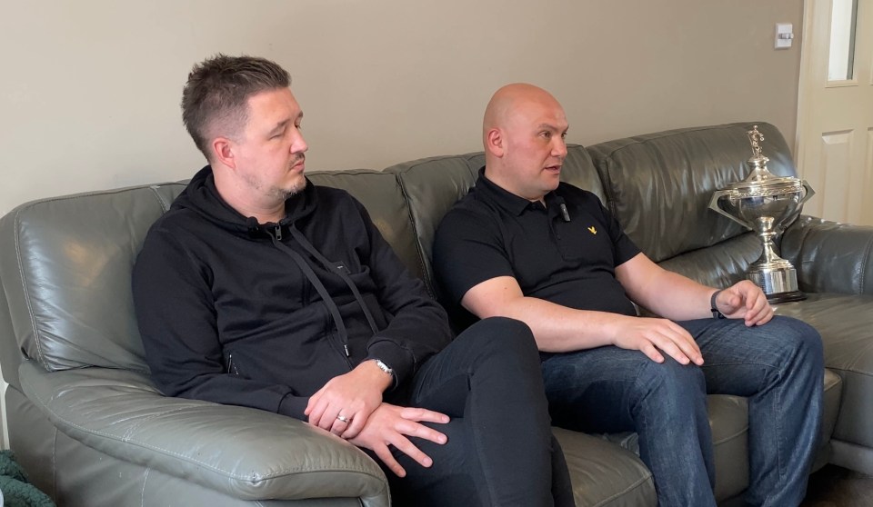 Two men sitting on a couch, one holding a trophy.
