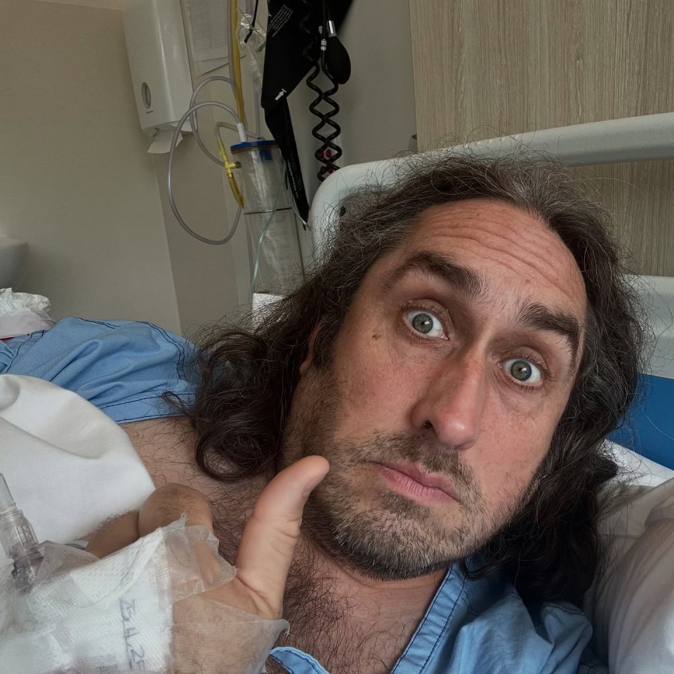 Ross Noble in a hospital bed giving a thumbs up.