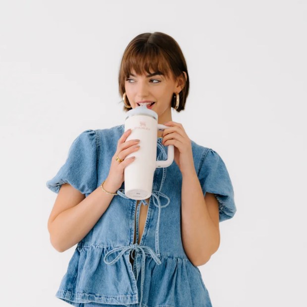 Woman in denim shirt drinking from a white Stanley tumbler.
