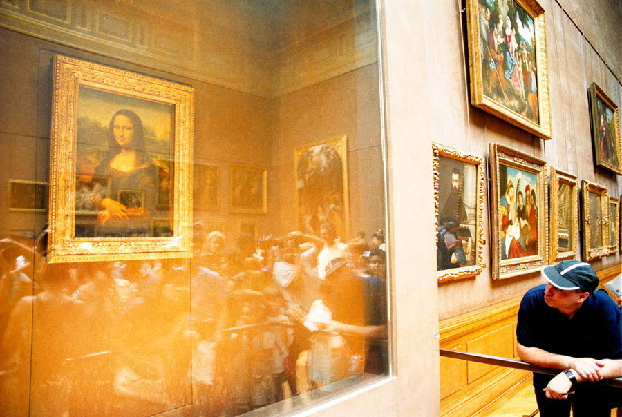 A man views the Mona Lisa through a protective glass case in a museum.