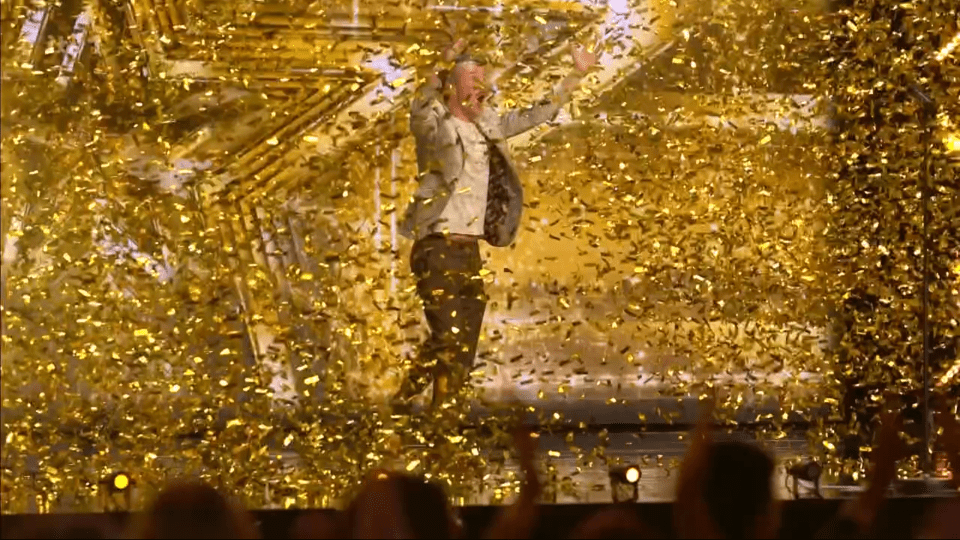 Person in a suit celebrating amidst falling gold confetti.