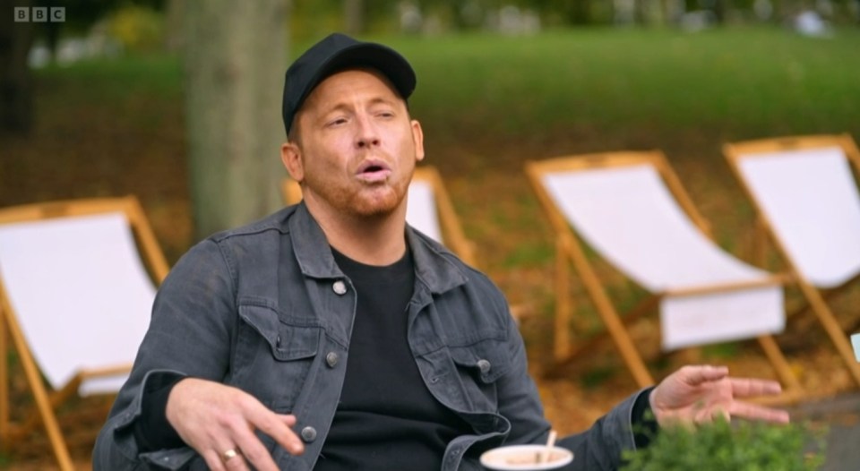 Man in a park talking, with deck chairs in the background.