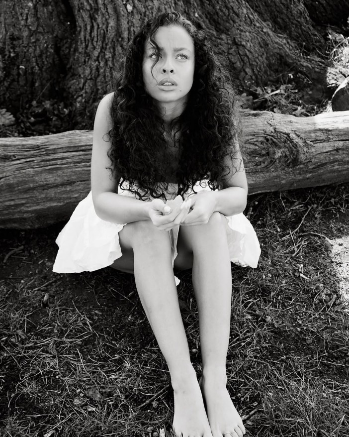 Black and white photo of a young woman sitting on the ground, looking up.