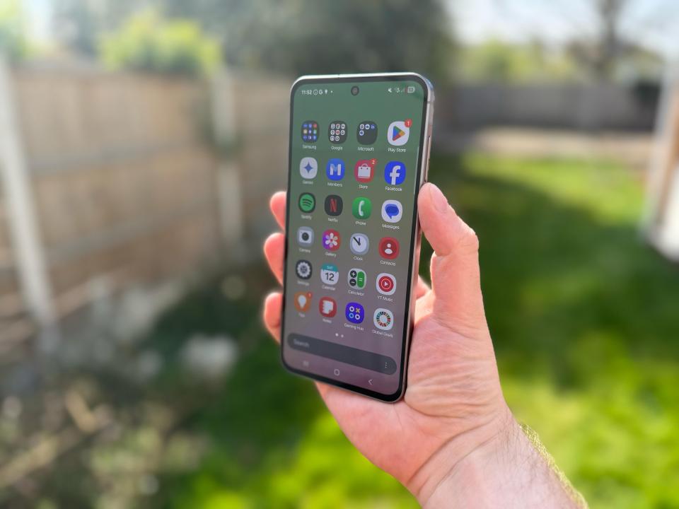 Hand holding smartphone displaying various app icons.