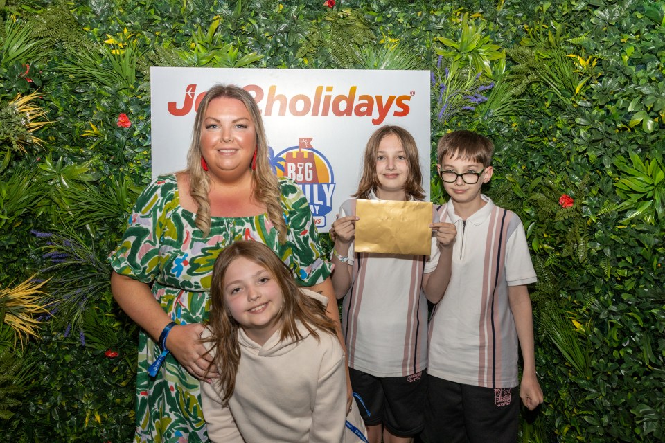 A family of five posing for a photo in front of a green wall and a "Big Family Getaway" sign.