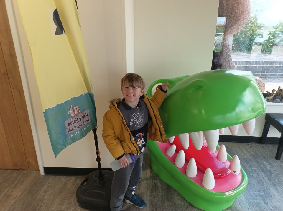 Boy standing by large dinosaur mouth sculpture.