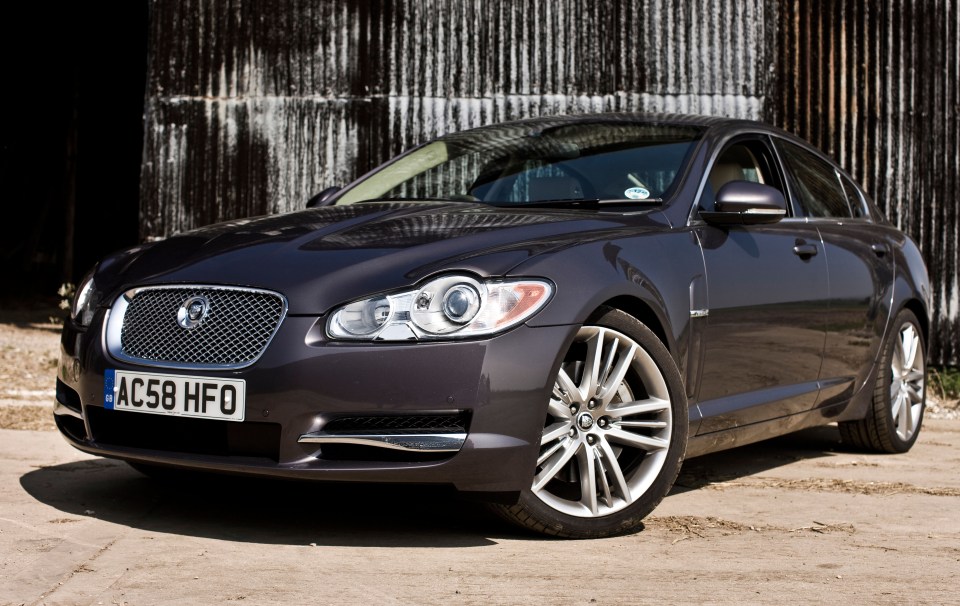 Dark gray Jaguar XFR parked in front of a corrugated metal wall.
