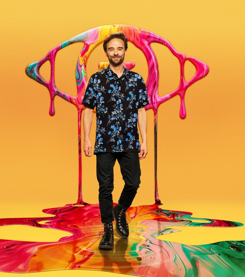 Jack P. Shepherd walking in front of a large, abstract paint splatter design resembling an eye.