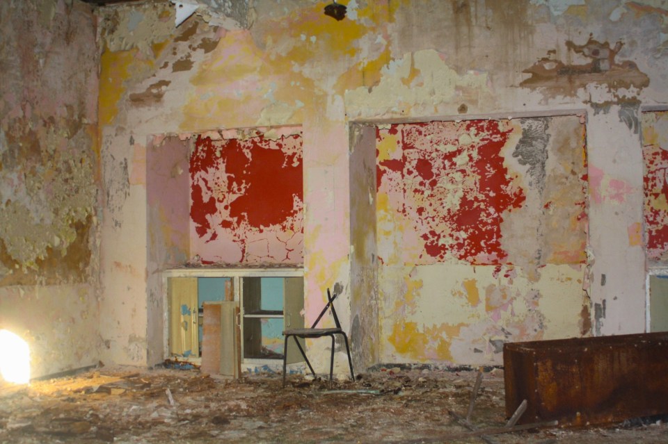 Interior of a dilapidated building with peeling paint and a chair.