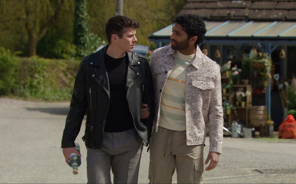 Two men walking and talking, one carrying a bottle.