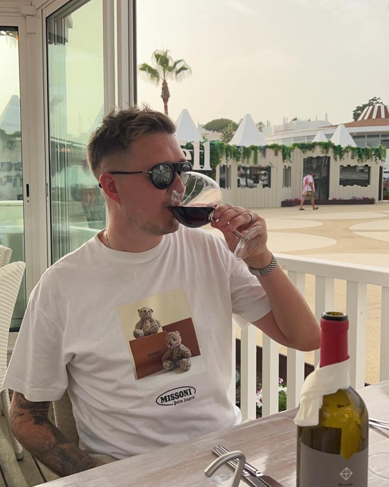 Man drinking red wine outdoors while wearing a Missoni Palm Angels t-shirt.