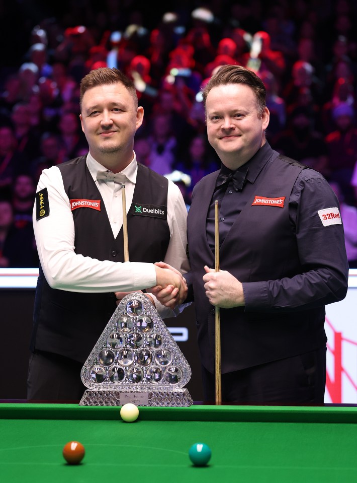Kyren Wilson and Shaun Murphy shaking hands at a snooker tournament.