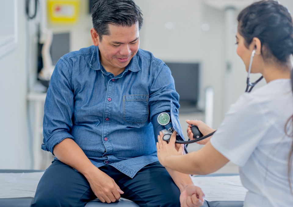 A doctor taking a middle-aged Asian man's blood pressure.