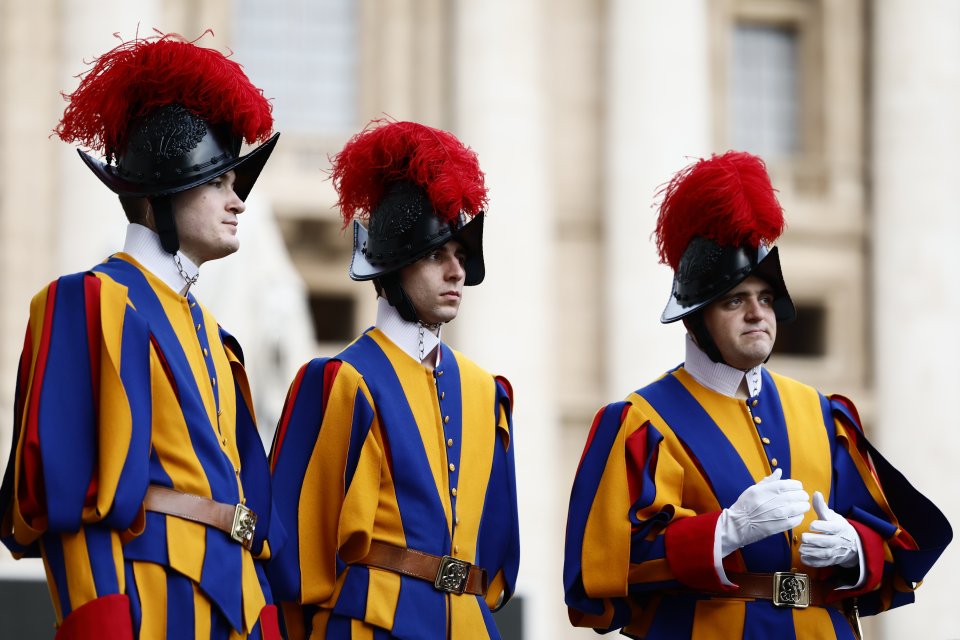 Three Swiss Guards in uniform stand outside St. Peter's Basilica.