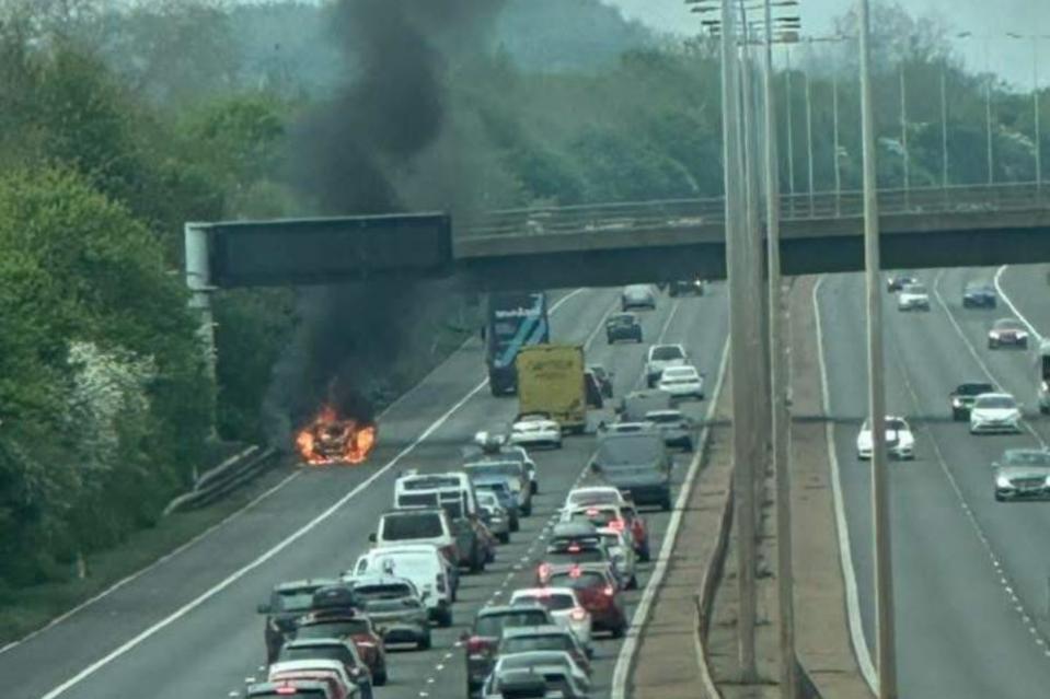 Car engulfed in flames on a highway, causing traffic backup.