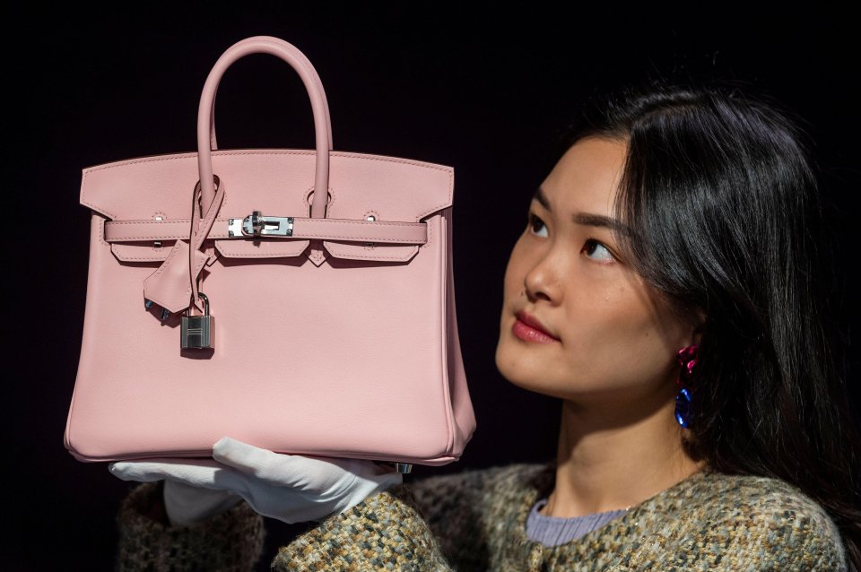 A staff member holding a pink Hermès Birkin handbag at a preview of an upcoming designer handbag auction.