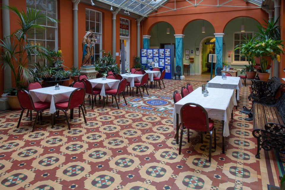 Cafe in a convent atrium with patterned tile floor and tables.