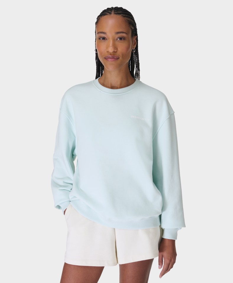 Woman in light blue sweatshirt and white shorts.