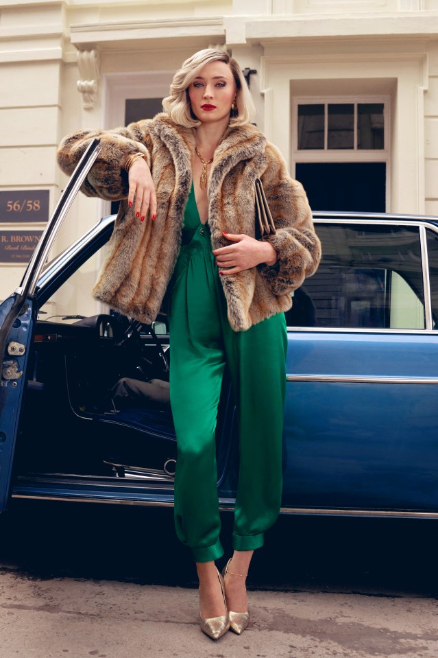 Sophie Turner as Joan in a fur coat and green jumpsuit, leaning against a vintage car.