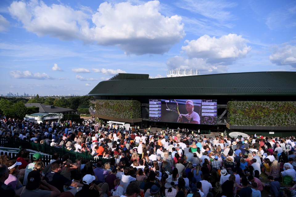 Large crowd watching a tennis match on a large screen at Wimbledon.