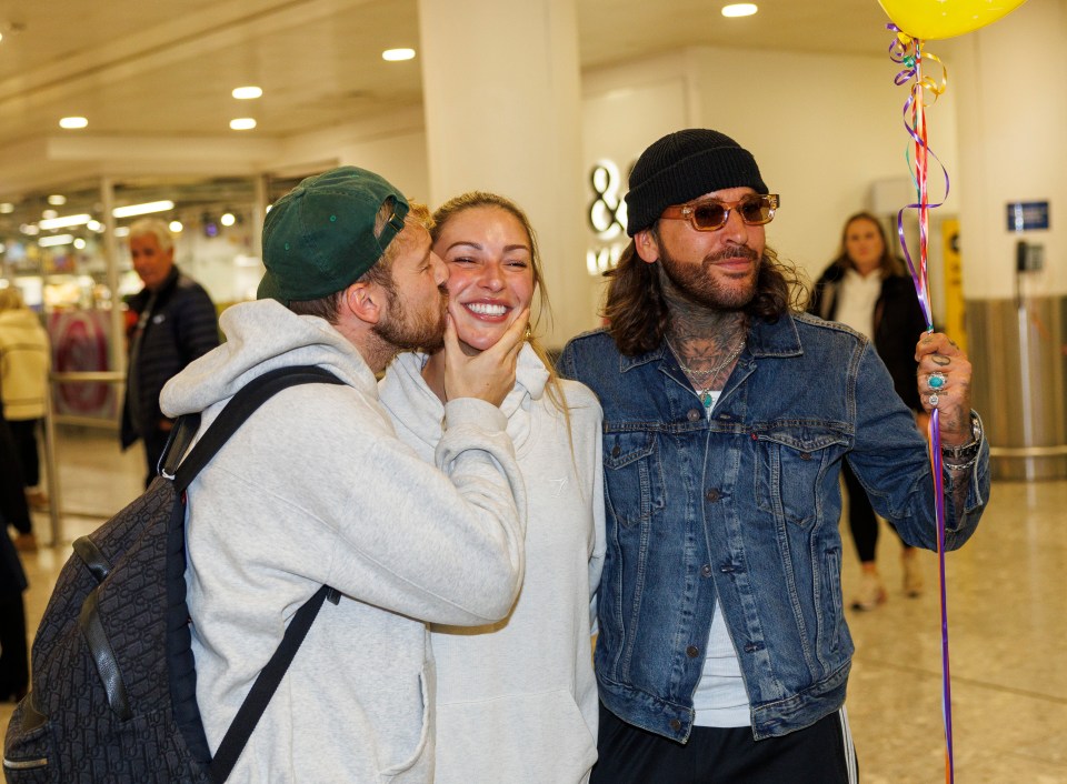 A man kissing a woman on the cheek, while another man holds a balloon.