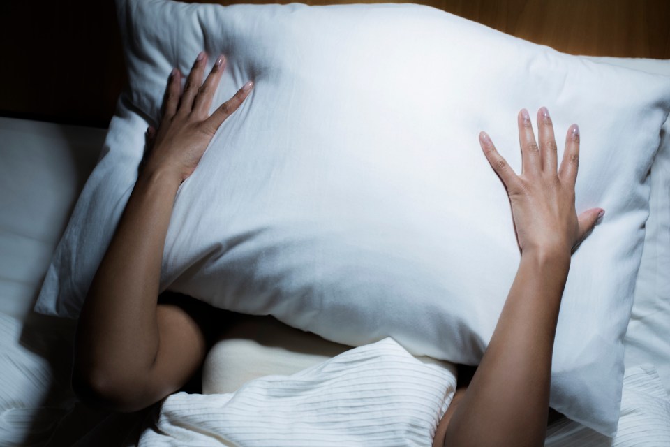 Woman in bed hiding her face under a pillow.