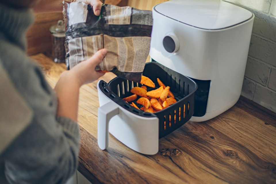 Woman pouring potato wedges into an air fryer.