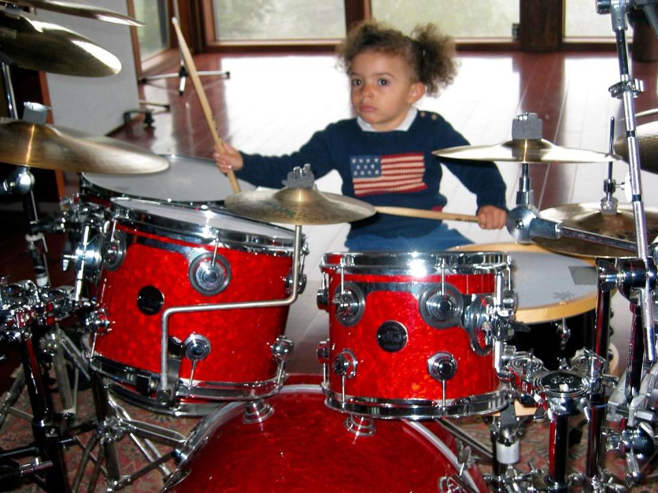 Young girl playing a red drum set.