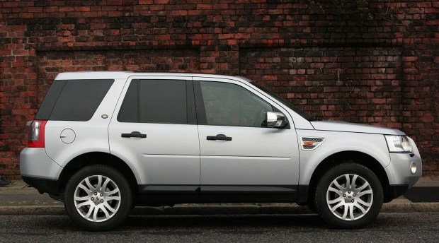 Silver Land Rover Freelander parked on a street next to a brick wall.
