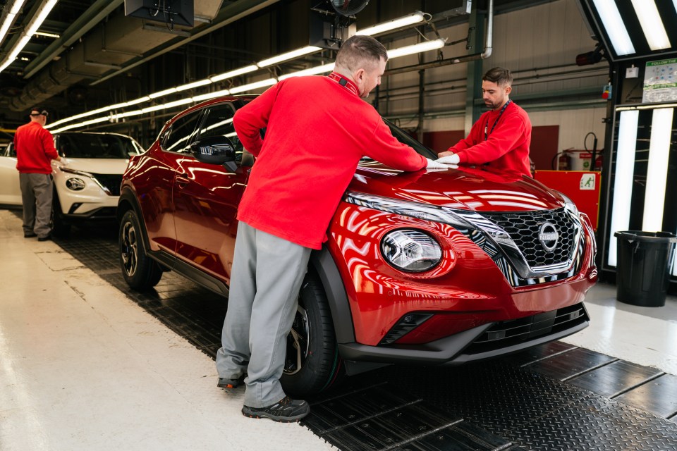 Workers inspecting a red Nissan Juke on a factory production line.