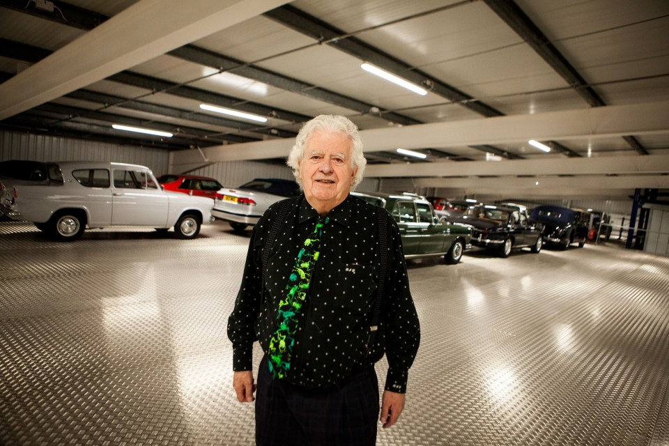 Man standing in a large garage with a collection of classic cars.