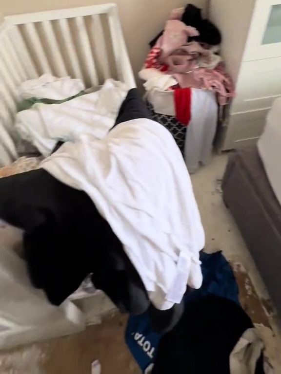 Overcrowded bedroom with baby crib and overflowing piles of clothes; text overlay reads, "we don't have the money to get all the storage stuff".