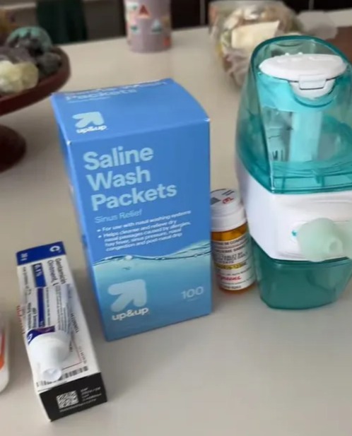 Saline wash packets, nasal wash bottle, and other medications on a table.