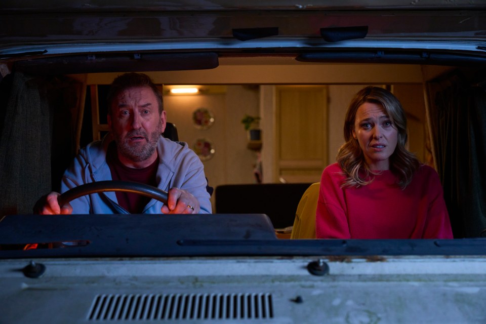 A man and woman sitting in the front seats of a campervan.