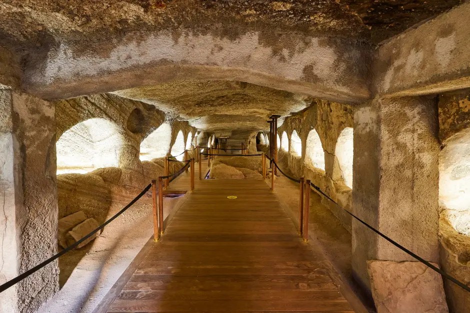 Wooden walkway through an ancient stone tunnel with alcoves.