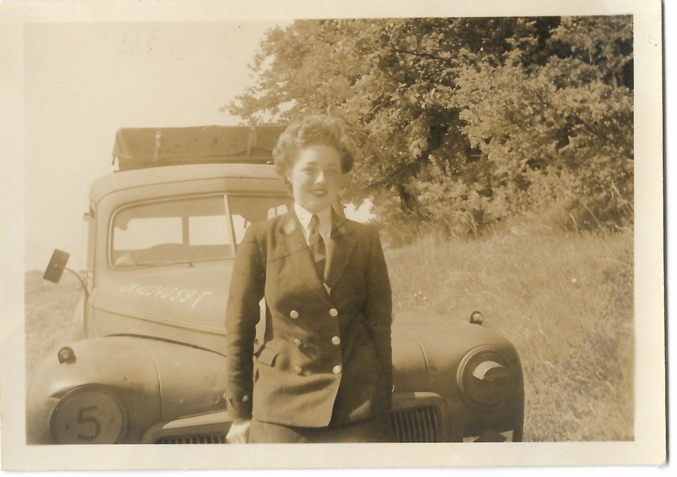 Woman in uniform standing in front of a vintage truck.