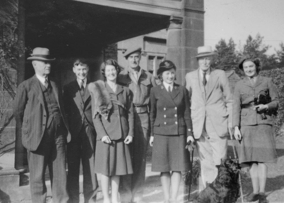 Black and white photo of seven people posing outside a building.