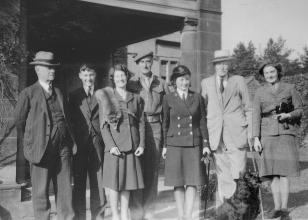 Black and white photo of seven people posing outside a building.