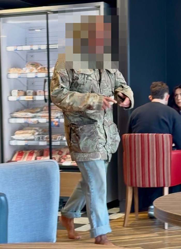 Person in camouflage jacket and jeans walking barefoot in a cafe.