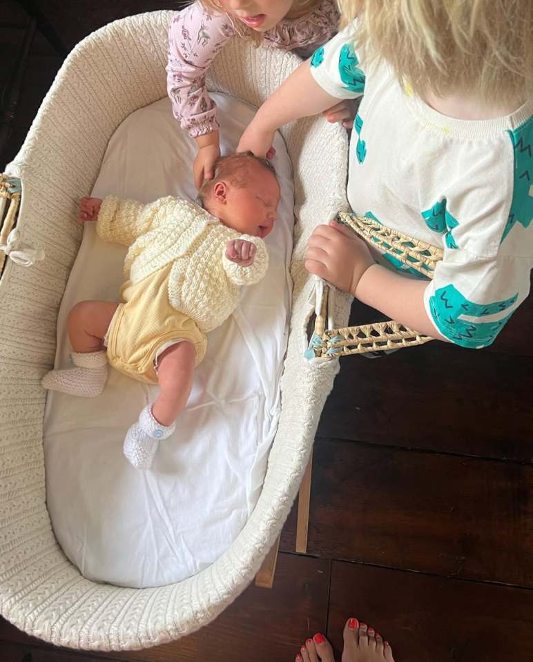 Two children looking at a newborn baby in a bassinet.