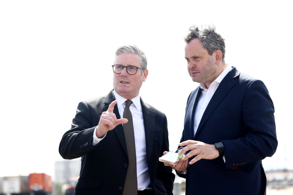 Two men in suits discussing something, one pointing.