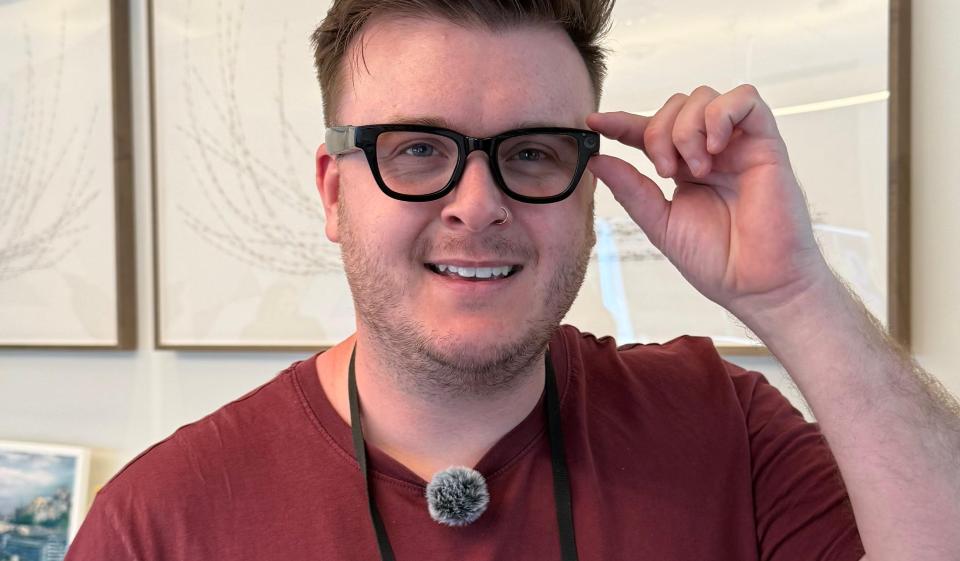 Man wearing glasses and a maroon shirt adjusts his glasses.