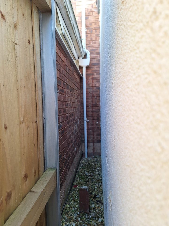 A narrow gap between two houses showing a section of fence and a drainpipe.