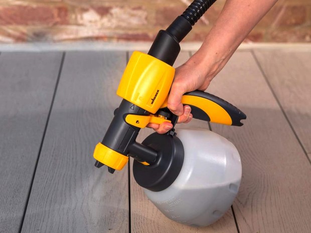 Person using a Wagner paint sprayer on a deck.