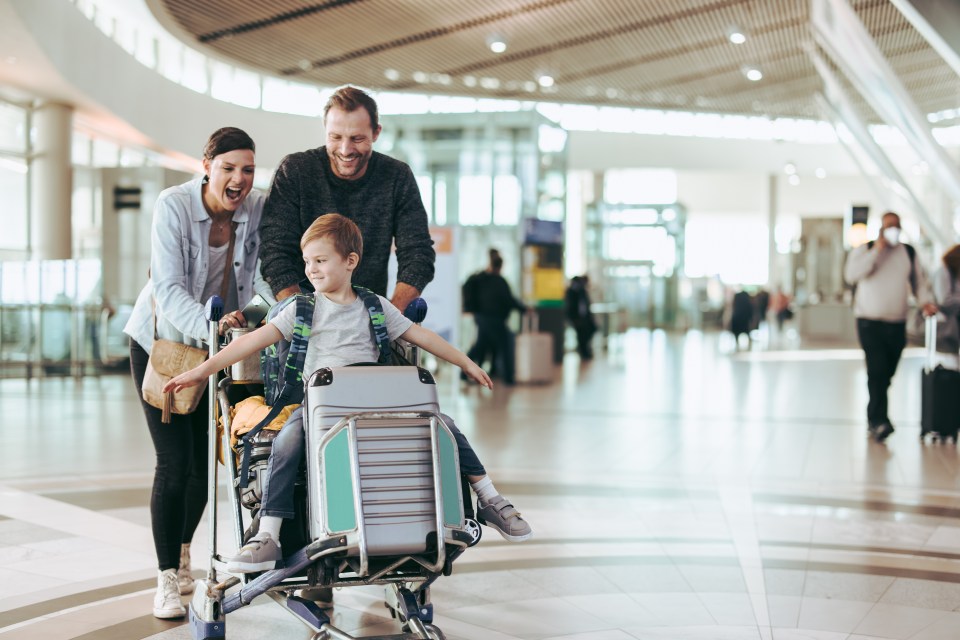 Family happily pushing a luggage trolley with their son at the airport.