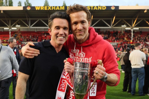 Rob McElhenney and Ryan Reynolds holding a trophy at a Wrexham football match.