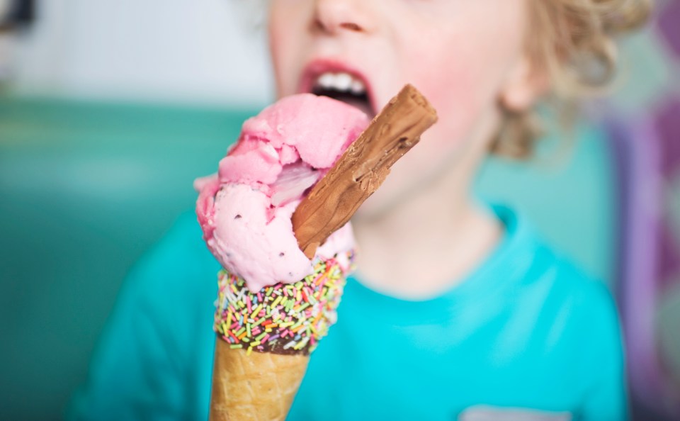 Child eating strawberry ice cream cone with sprinkles and a chocolate bar.