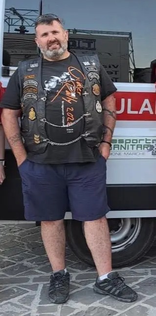 Man in motorcycle vest standing in front of an ambulance.
